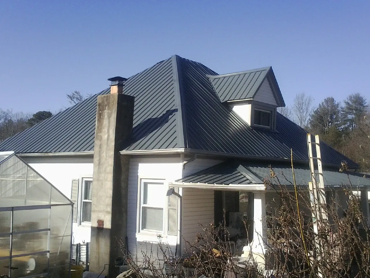 Dark blue standing seam metal roof on a white farmhouse with dormer — Slate & Tile Roof Repair by Roofing Brothers in Crystal Beach