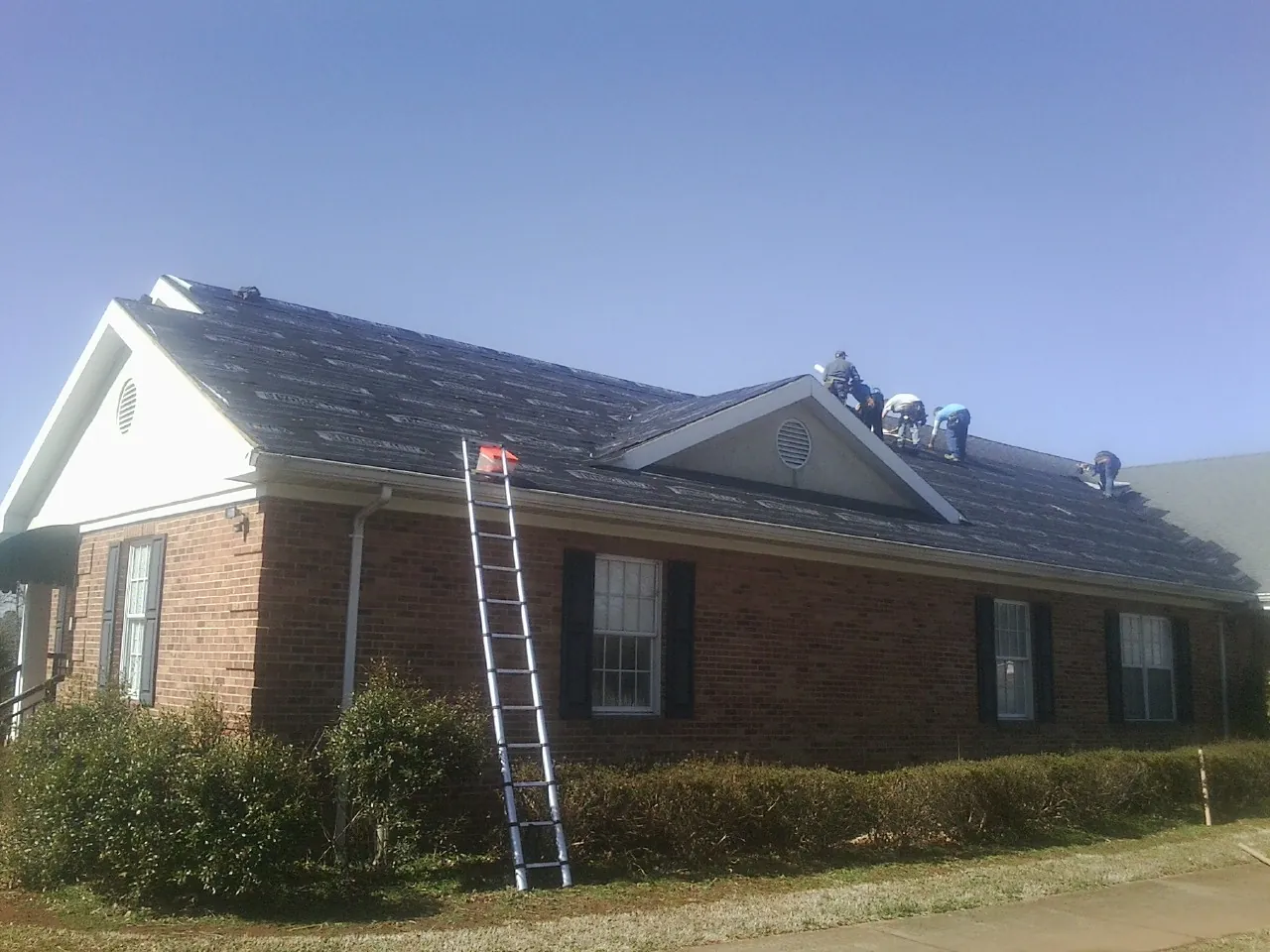 Crew tearing shingles off a brick ranch roof with a ladder set — Emergency Roof Repair work by our crew in Crystal Beach