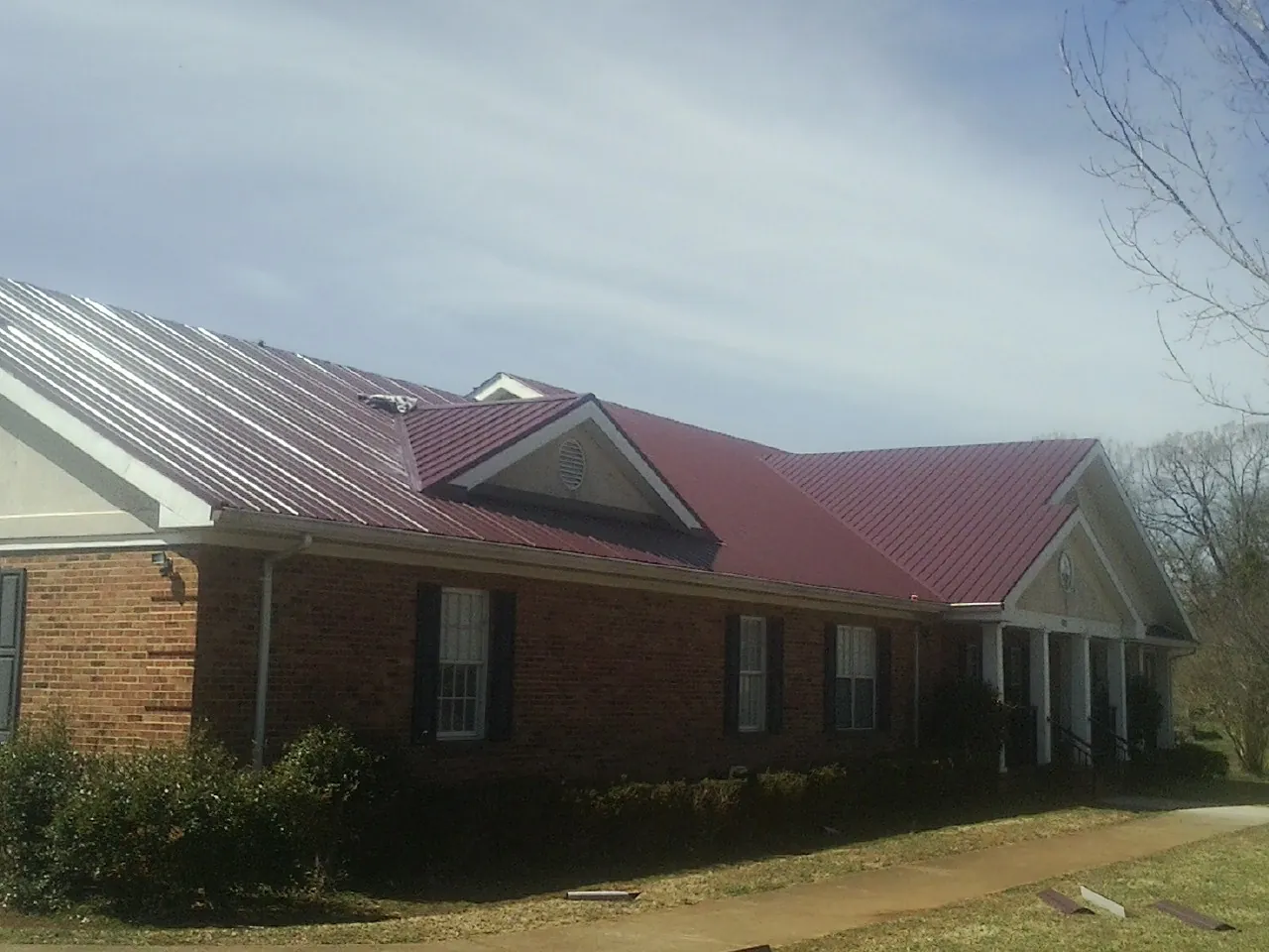 Red metal roof with gabled entries on a long brick building, from a Hail Damage Roof Repair job in Crystal Beach