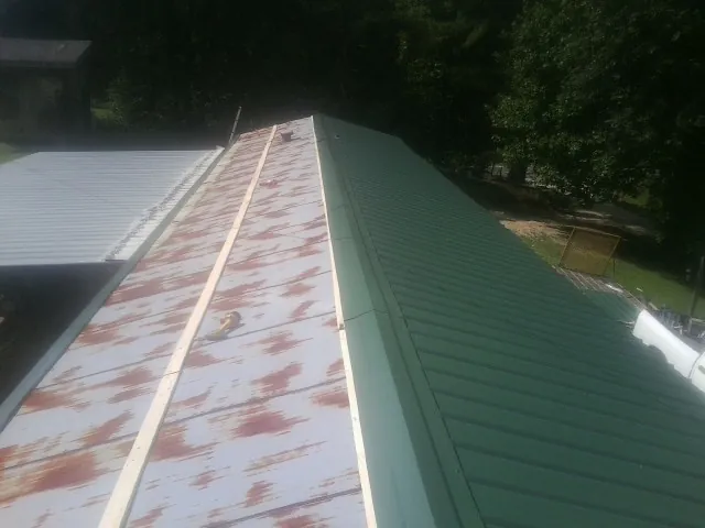 Old rusted panels beside newly installed green metal roofing — Wind Damage Roof Repair by Roofing Brothers in Crystal Beach