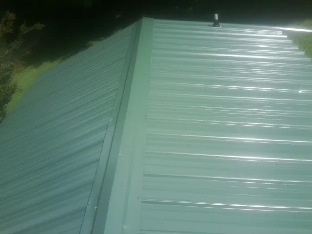New green metal panels meeting at the ridge of a roof — Flat Roof Repair work by our crew in Crystal Beach