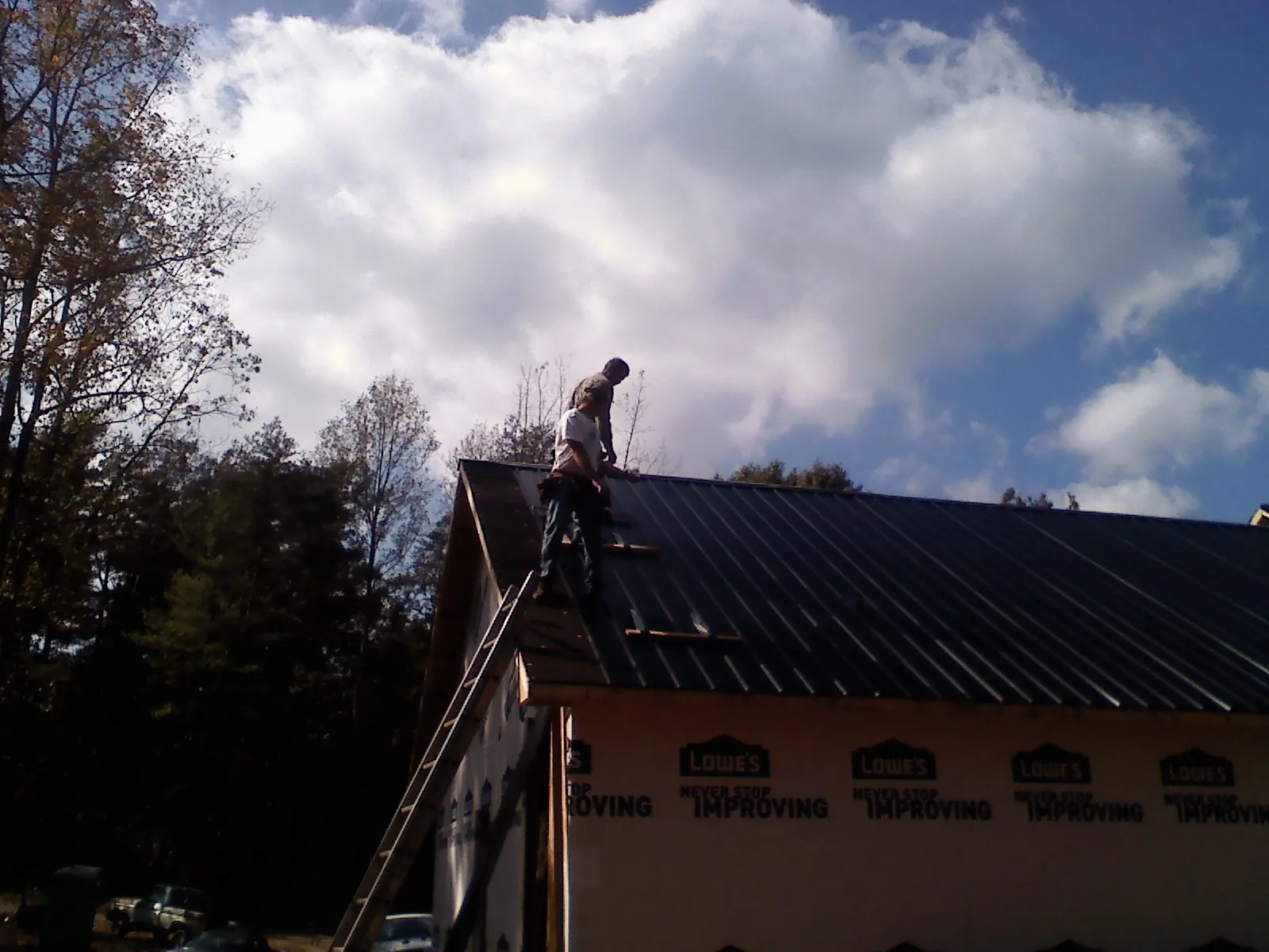 Roofer fastening dark metal panels high against a cloudy sky, from a Roof Inspection job in Crystal Beach