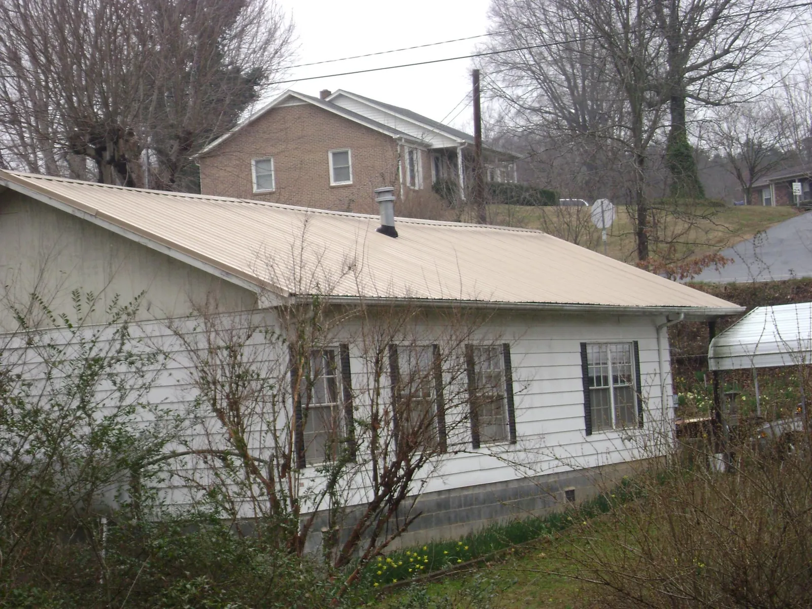 Tan metal roof on a white sided house set into a hillside — Commercial Roofing by Roofing Brothers in Crystal Beach