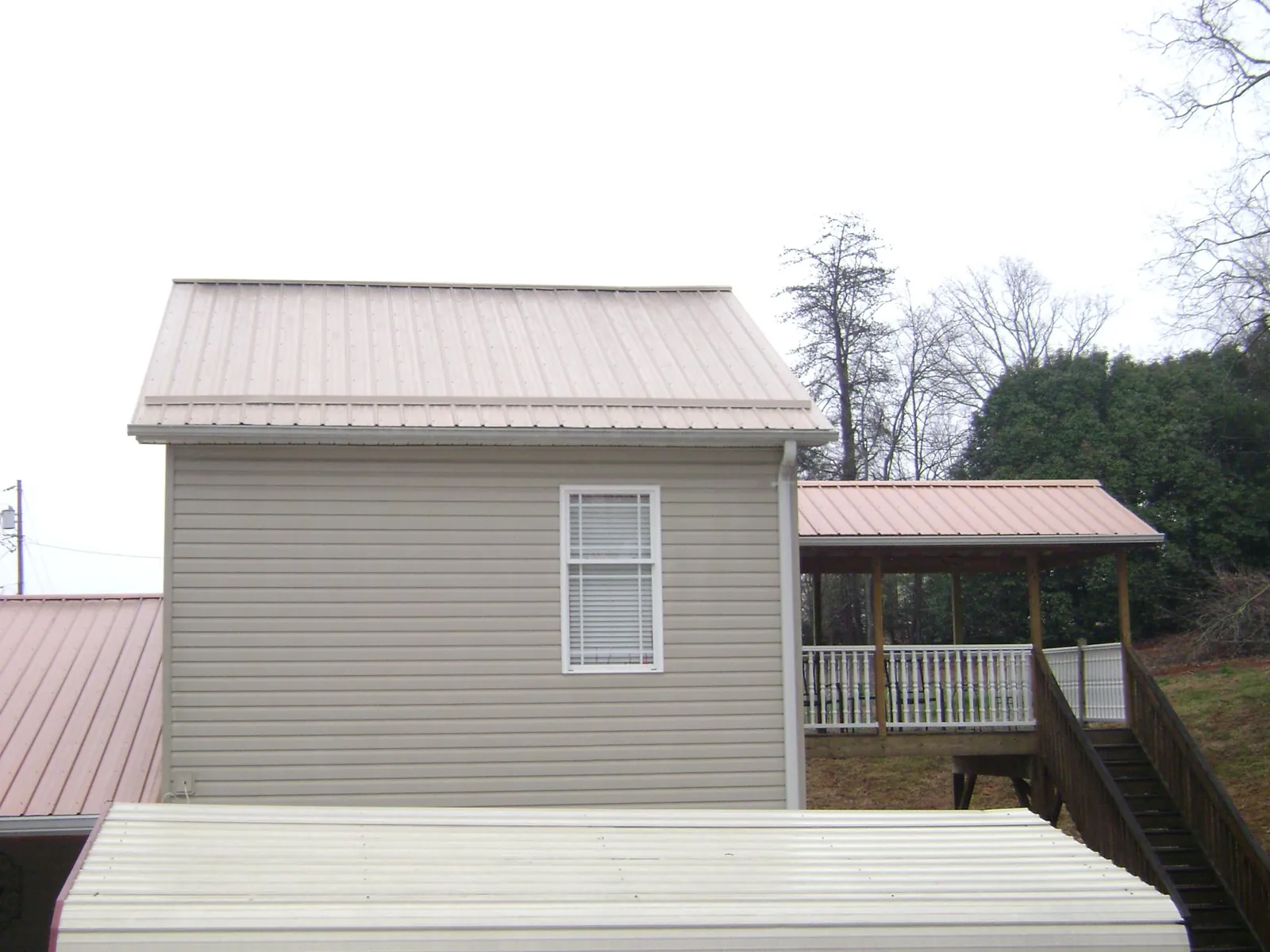 Tan metal roofs on a two story addition and attached porch, from a Roof Replacement job in Crystal Beach